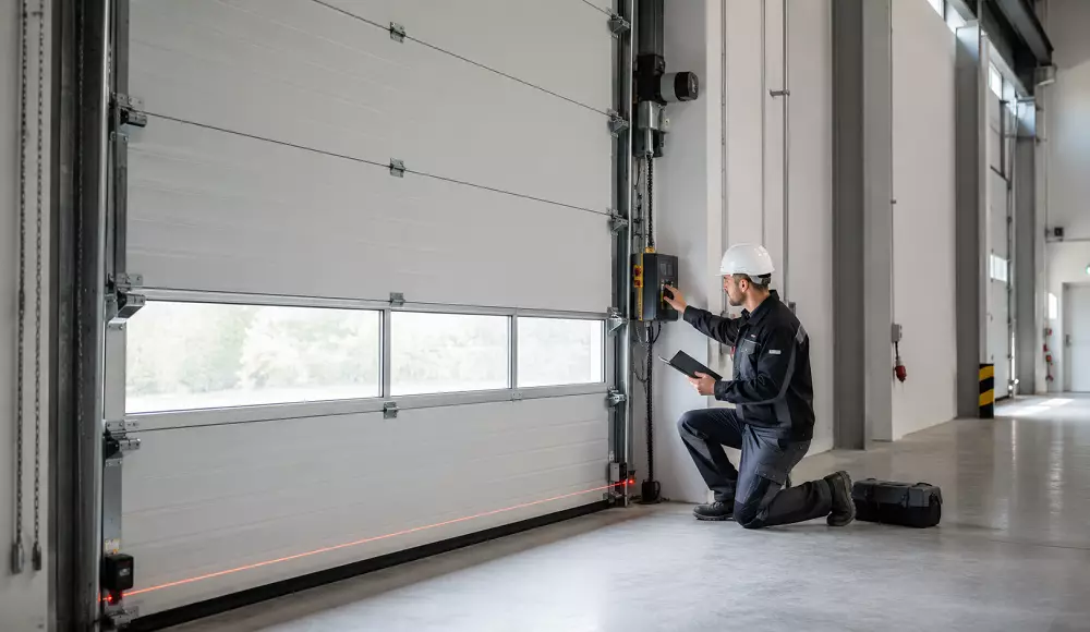 Prüfer kontrolliert ein kraftbetätigtes Sektionaltor in einer Industriehalle und dokumentiert die sicherheitstechnische sowie elektrische Prüfung der Toranlage.
