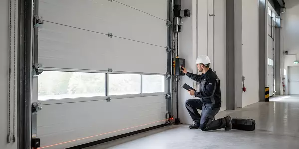 Prüfer kontrolliert ein kraftbetätigtes Sektionaltor in einer Industriehalle und dokumentiert die sicherheitstechnische sowie elektrische Prüfung der Toranlage.
