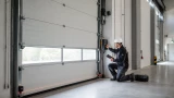 Prüfer kontrolliert ein kraftbetätigtes Sektionaltor in einer Industriehalle und dokumentiert die sicherheitstechnische sowie elektrische Prüfung der Toranlage.