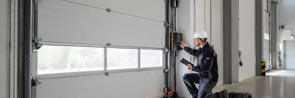 Prüfer kontrolliert ein kraftbetätigtes Sektionaltor in einer Industriehalle und dokumentiert die sicherheitstechnische sowie elektrische Prüfung der Toranlage.